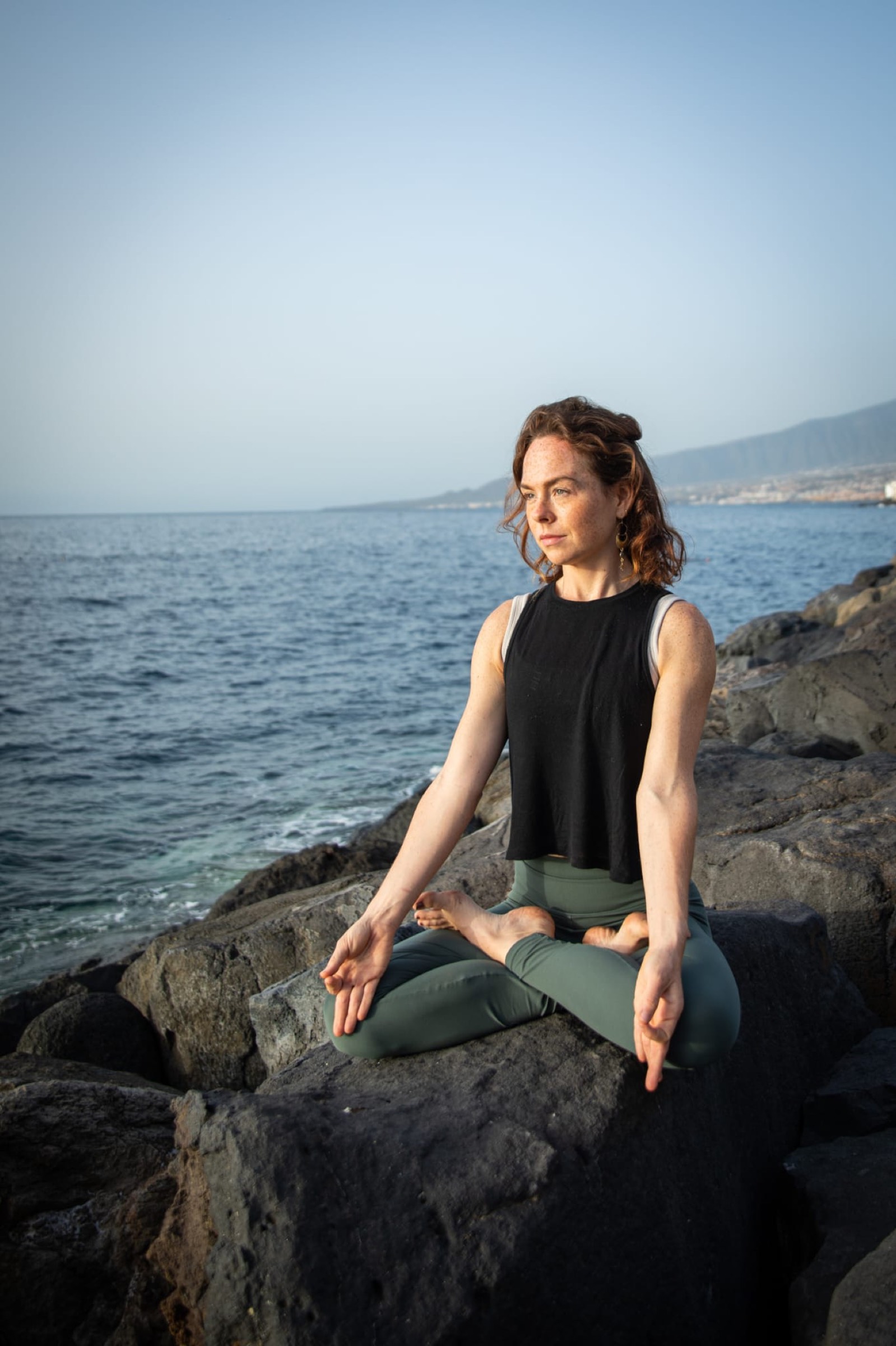 Natalie Bruce in meditation on volcanic rock above the sea in Tenerife