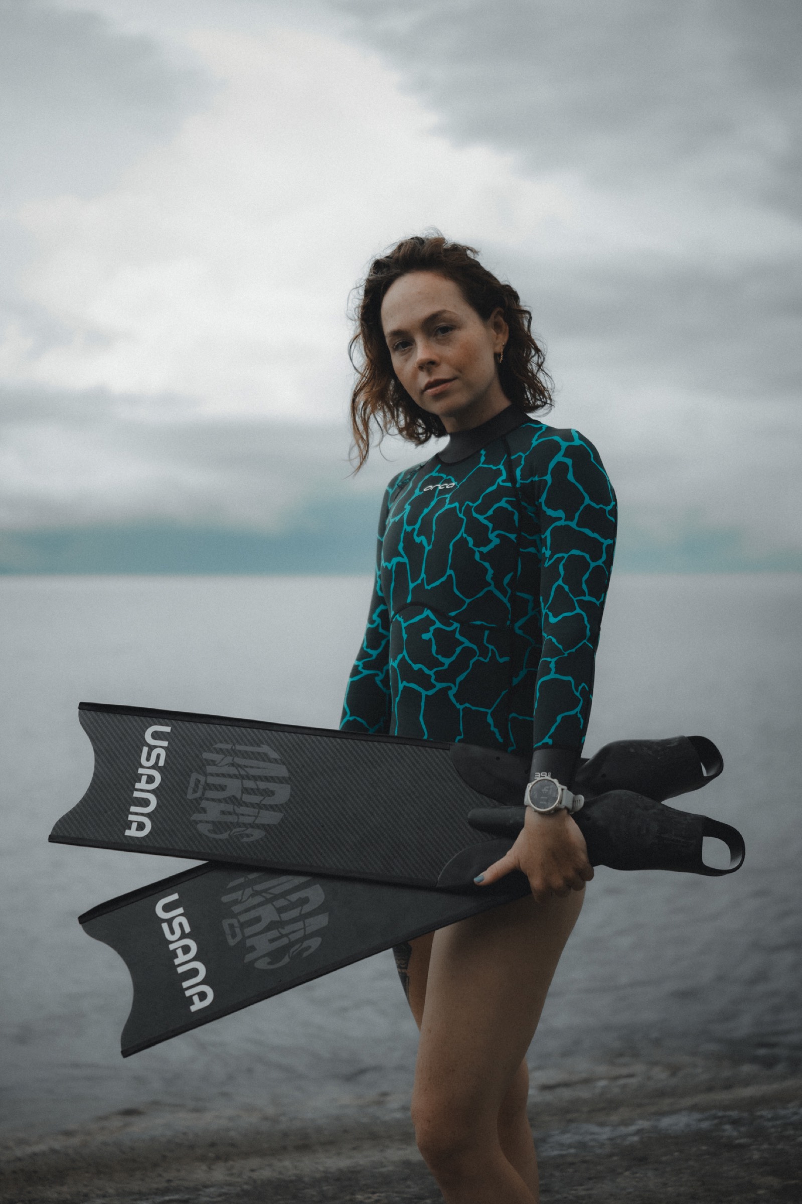 Natalie Bruce holding USANA freediving fins by the water