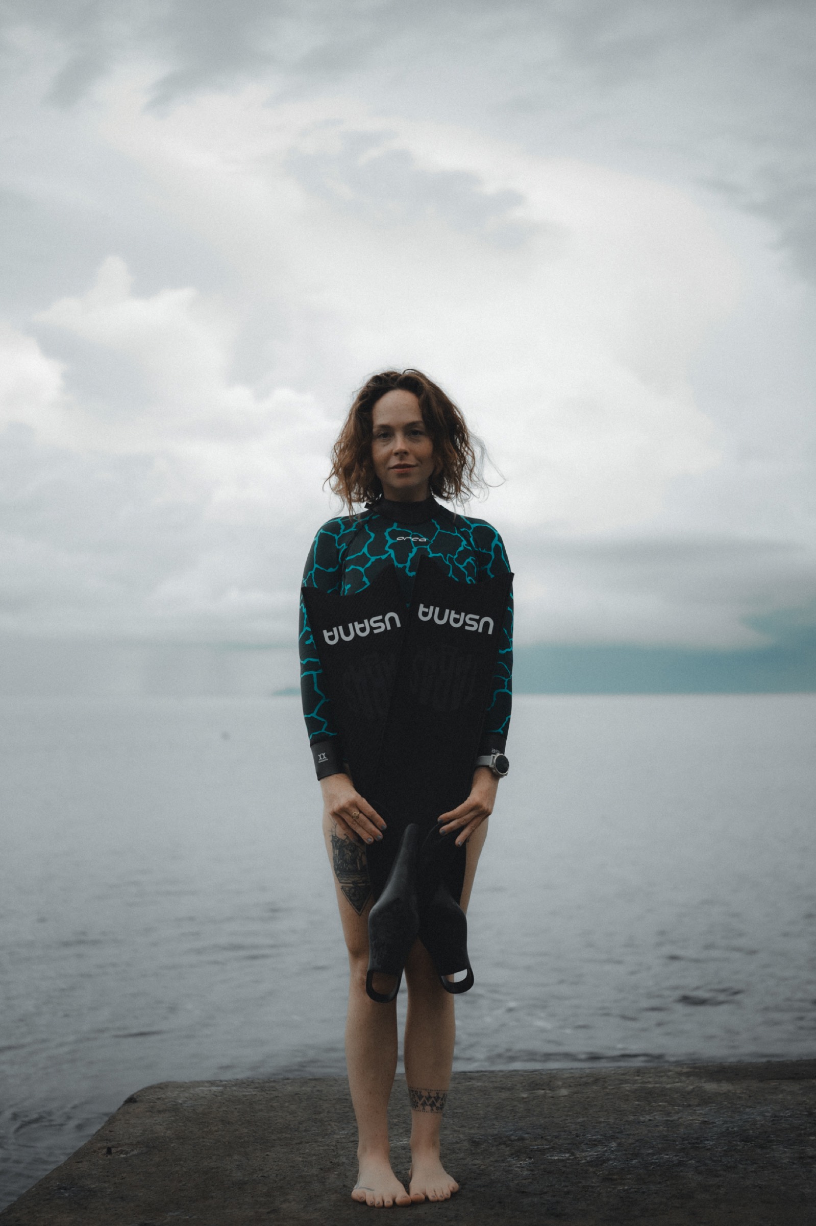 Natalie Bruce standing in USANA wetsuit on a quiet shoreline