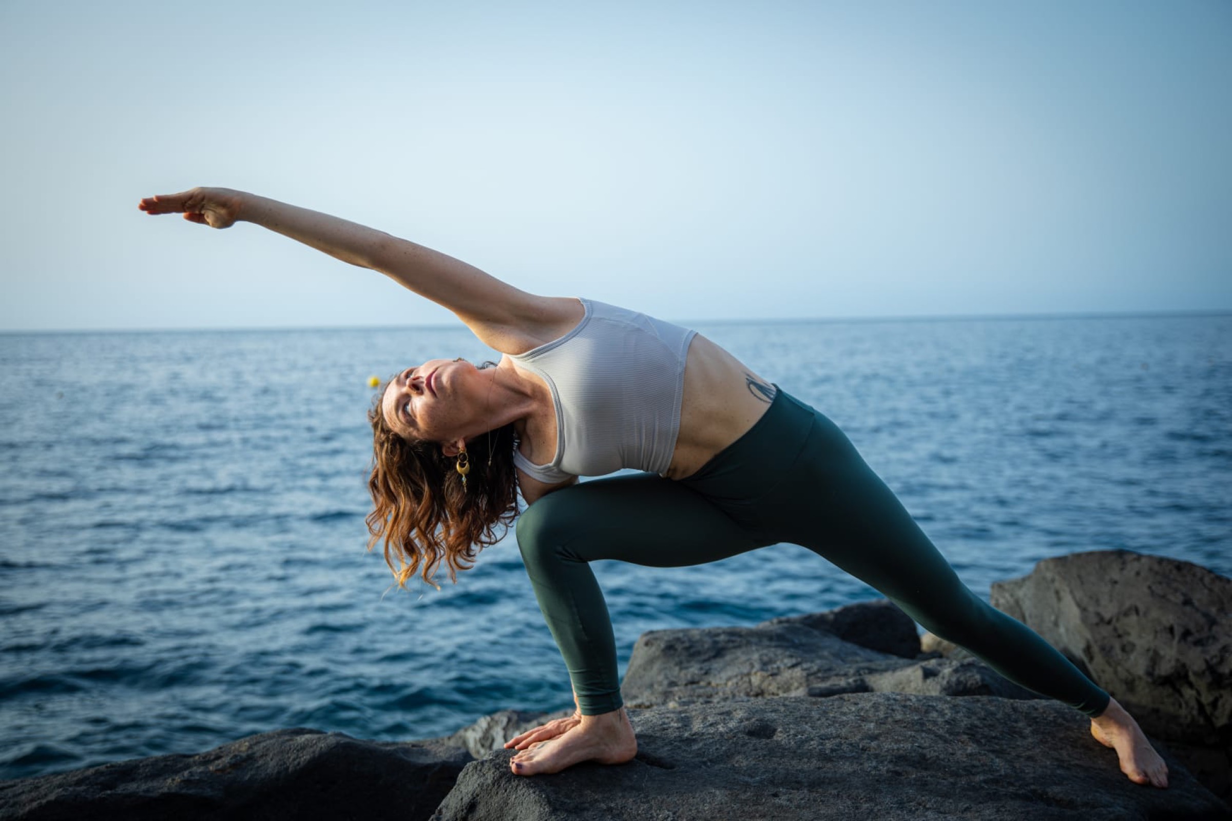 Natalie Bruce in a yoga side-angle pose on volcanic rock by the sea in Tenerife