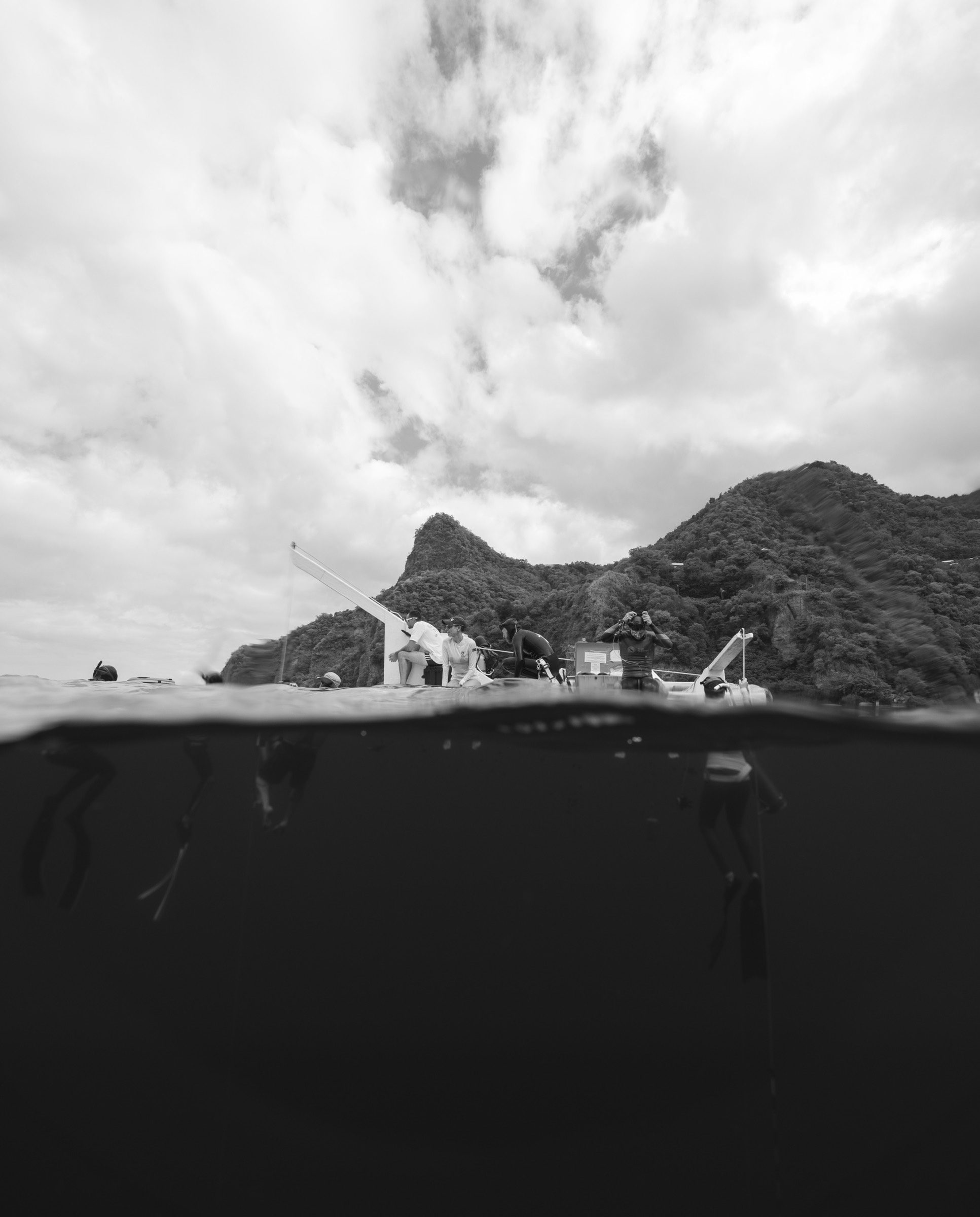 Black and white waterline view of the dive boat with crew and coastline behind