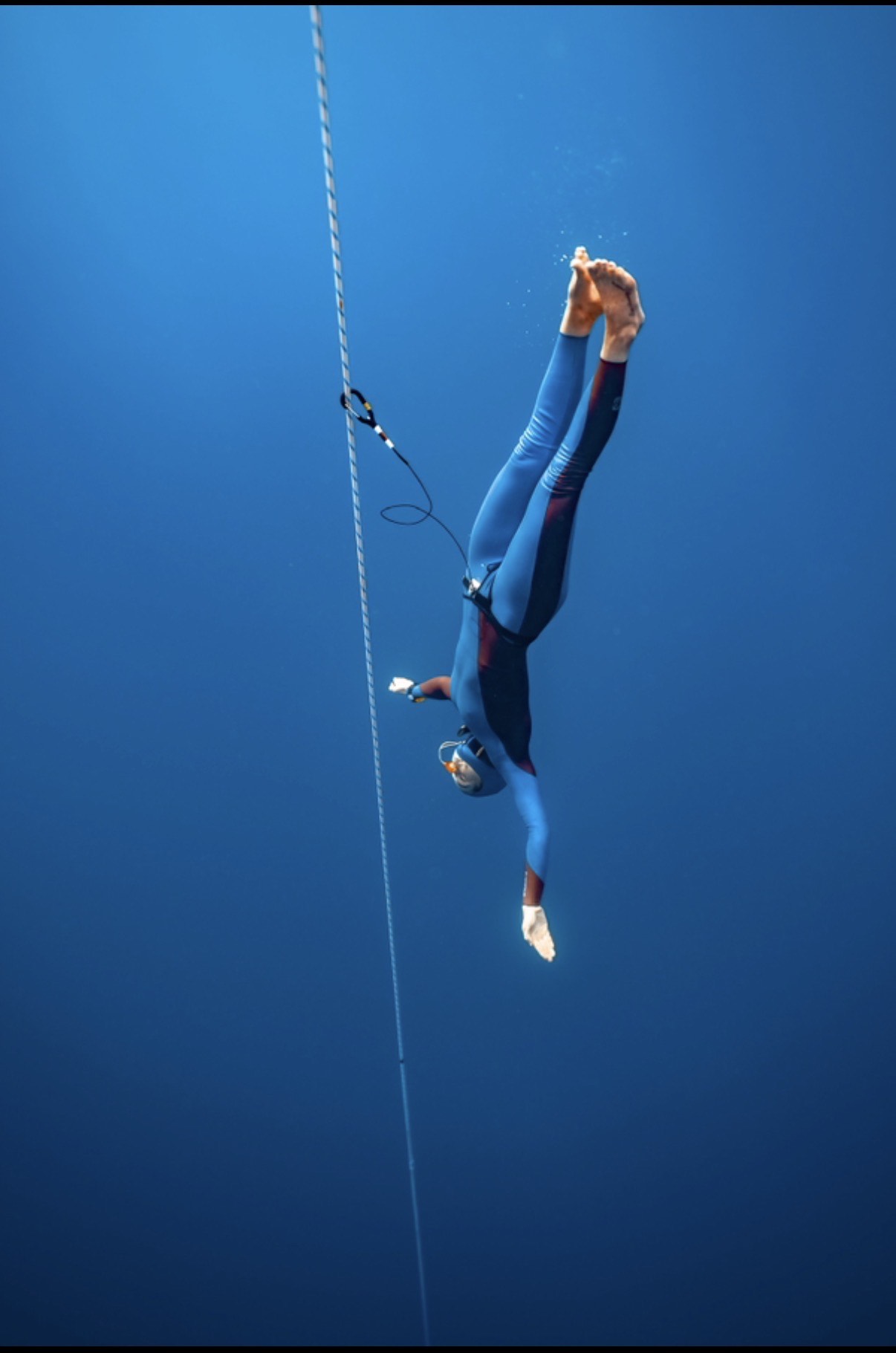 Natalie Bruce descending headfirst on the line in a blue wetsuit