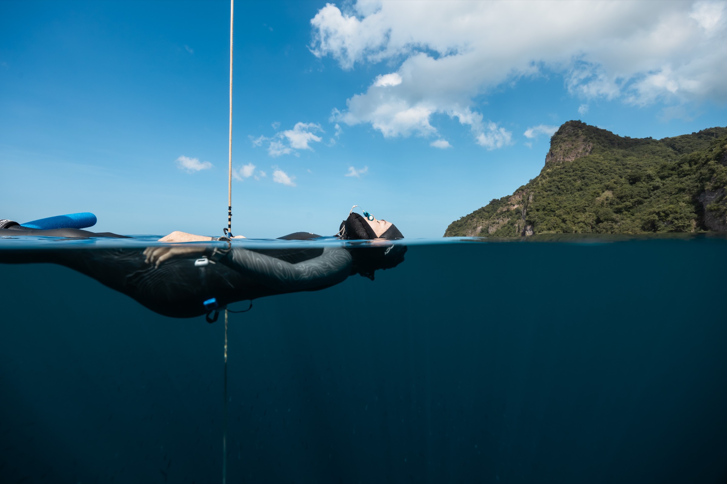 Natalie Bruce floating at the surface on the line between dives, coastline behind